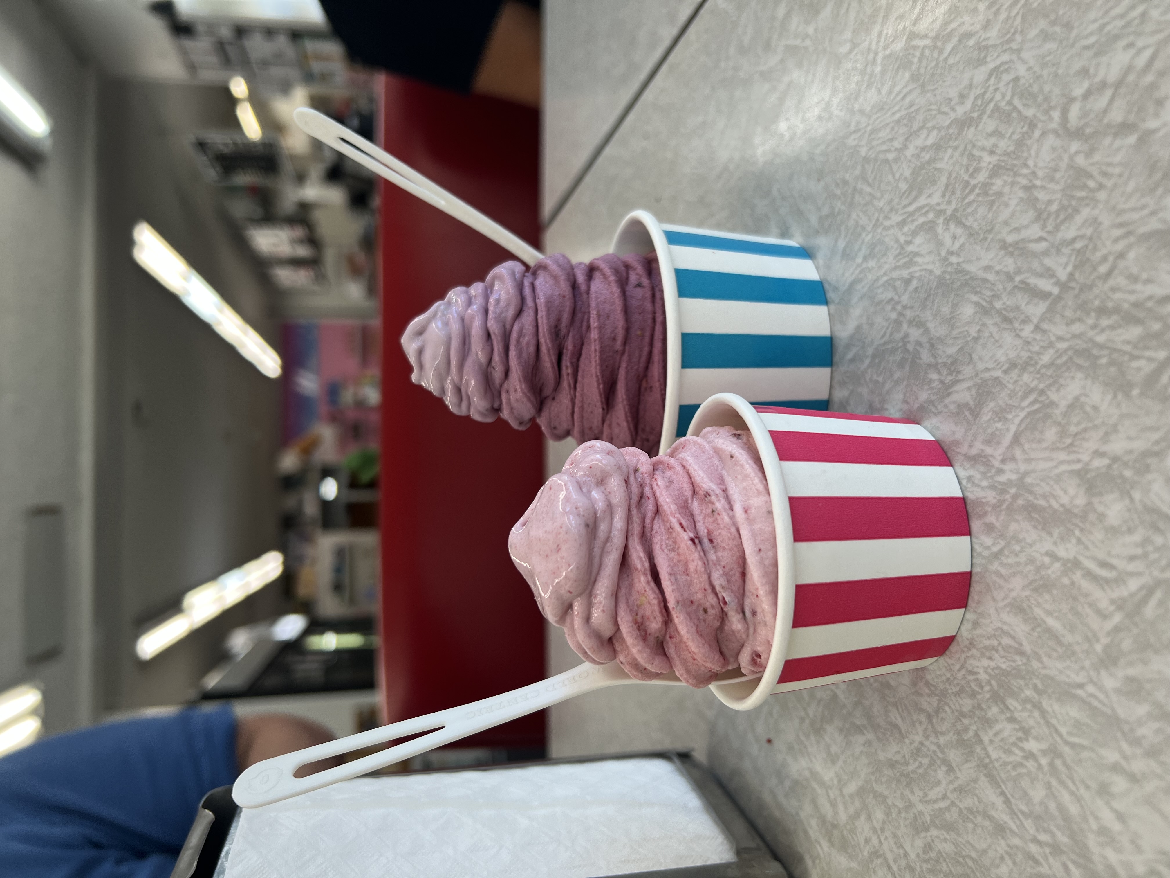 two cups of soft serve. On the left a pale pink swirl of strawberry soft serve, on the right a swirl of blackberry and strawberry for a gradient from deep purple to periwinkle.